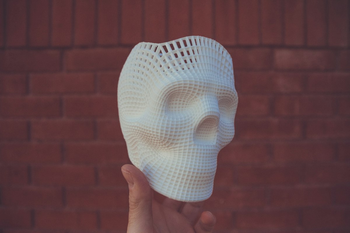 Mano sosteniendo un biomodelo anatómico de cráneo impreso en 3D en resina blanca, con estructura interna tipo retícula