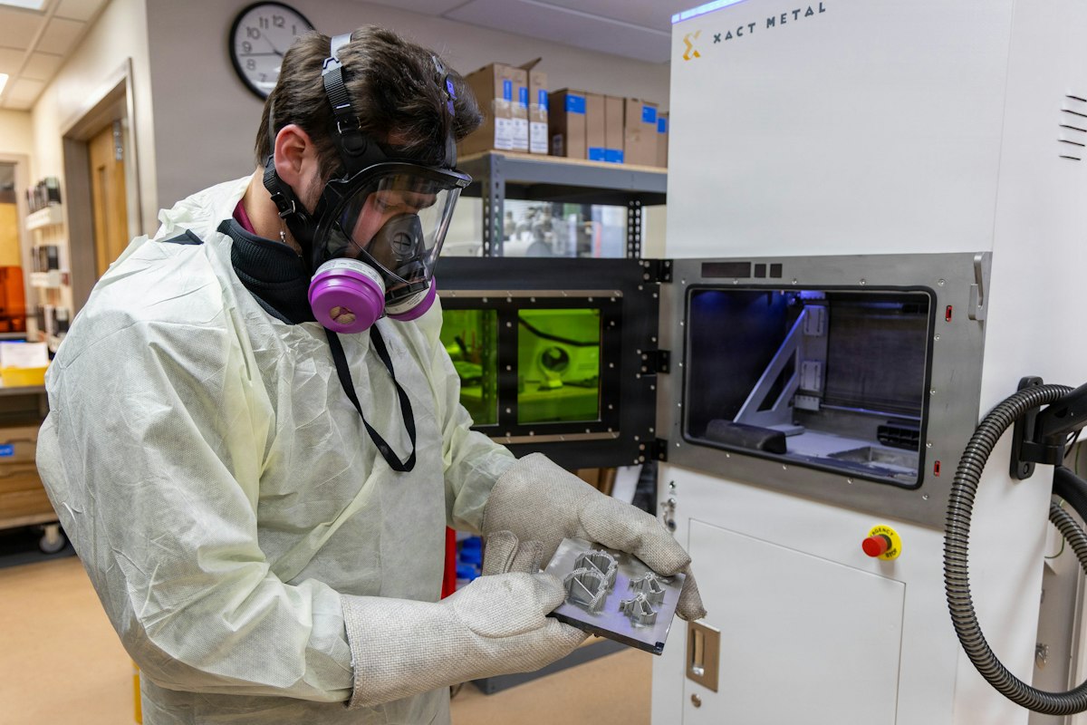 Ingeniero con equipo de protección inspecciona una plataforma con dispositivos dentales impresos en 3D junto a una impresora 3D de metal